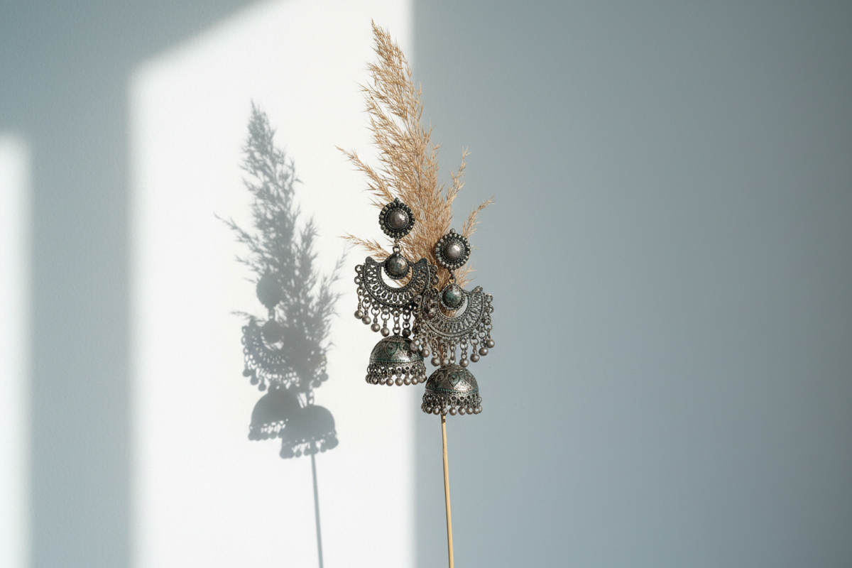 Oxidised silver jhumka earrings hanging from dried pampas grass in minimalist white studio — ethnic jewellery by Taniva